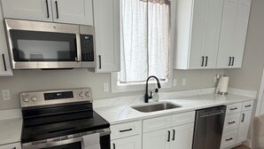 A modern kitchen with white cabinets, a stainless steel oven, a microwave, a sink, and a dishwasher.