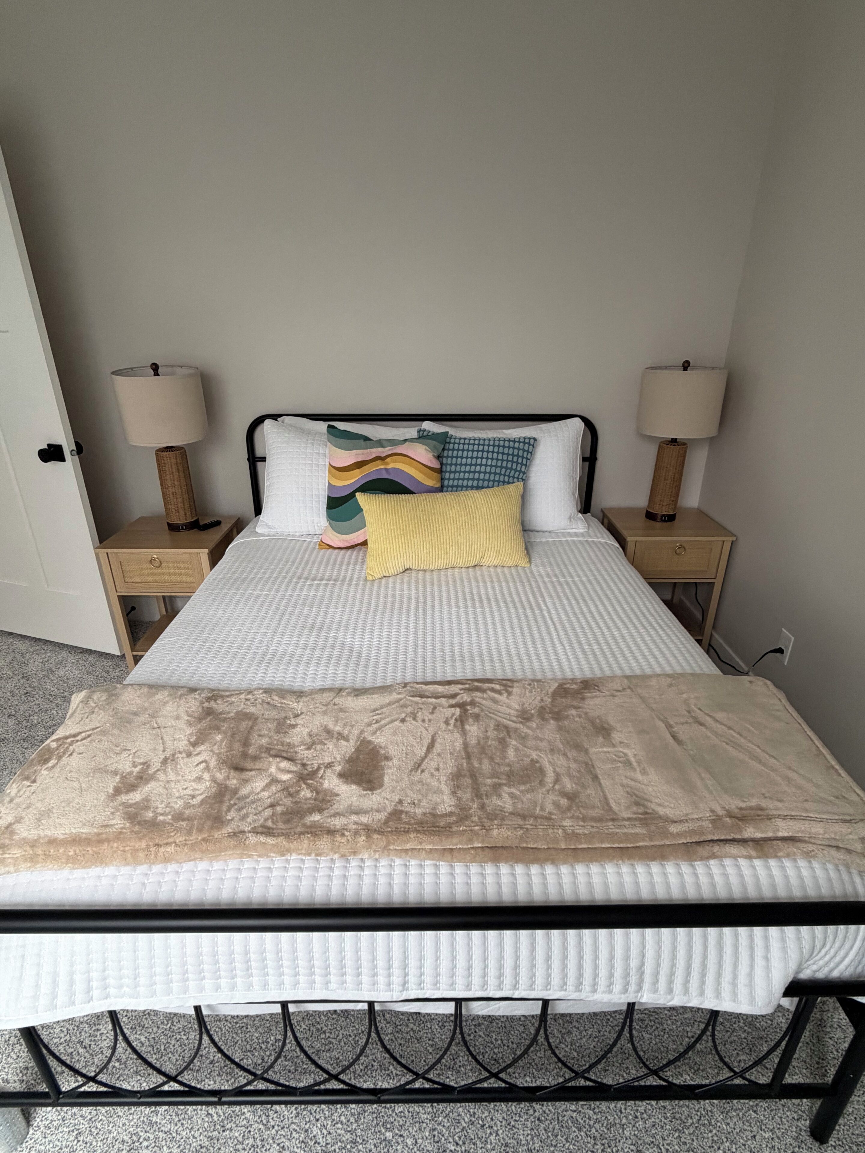A bed with a beige cover, two bedside tables with lamps, and a plain wall.
