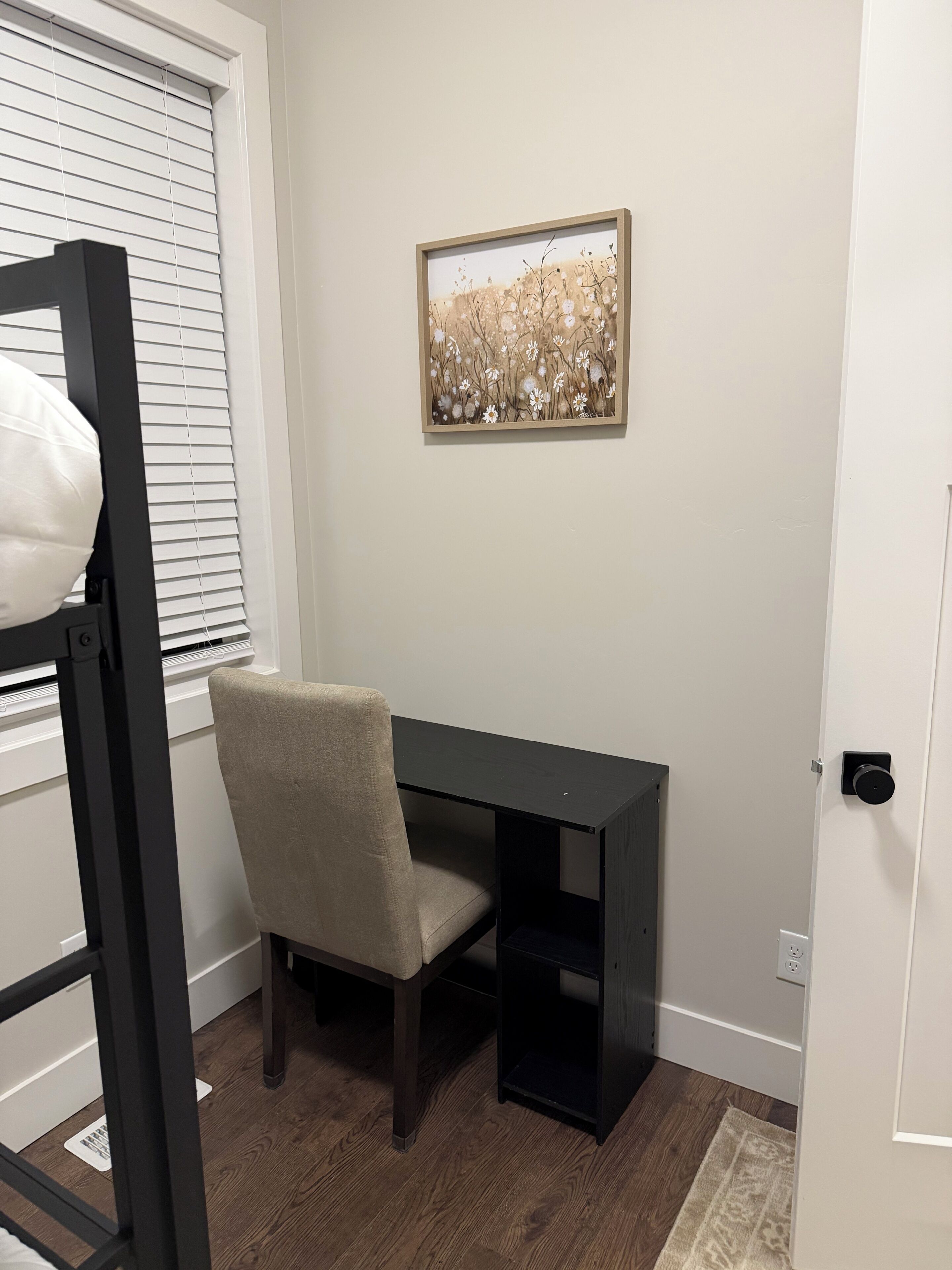 A room with a desk, chair, and a framed picture on the wall.