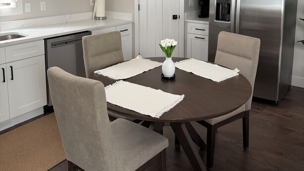 A modern kitchen with white cabinets, a stainless steel refrigerator, and a dining table with four chairs.