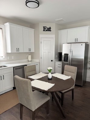 A modern kitchen with white cabinets, a stainless steel refrigerator, and a dining table with four chairs.