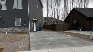 A residential area with a paved driveway, a house with a stone foundation, and a wooden fence.