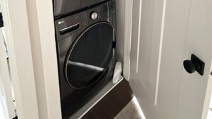 A laundry room with two stacked washing machines, a red box on top, and a white door.