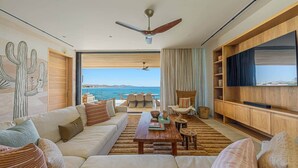 Una sala de estar con sofá, mesa de centro y televisor, ventilador de techo y vista al mar.