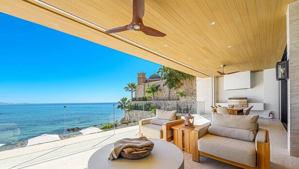 Un espacio exterior moderno con vistas al mar, una pared de piedra y un ventilador de techo de madera.