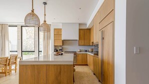 Una cocina moderna con armarios de madera, una isla central, iluminación colgante y vistas al exterior.