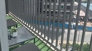 Een balkon met uitzicht op een meerhoog gebouw in aanbouw, een metalen hekwerk en een kleine tafel met een bloempot.