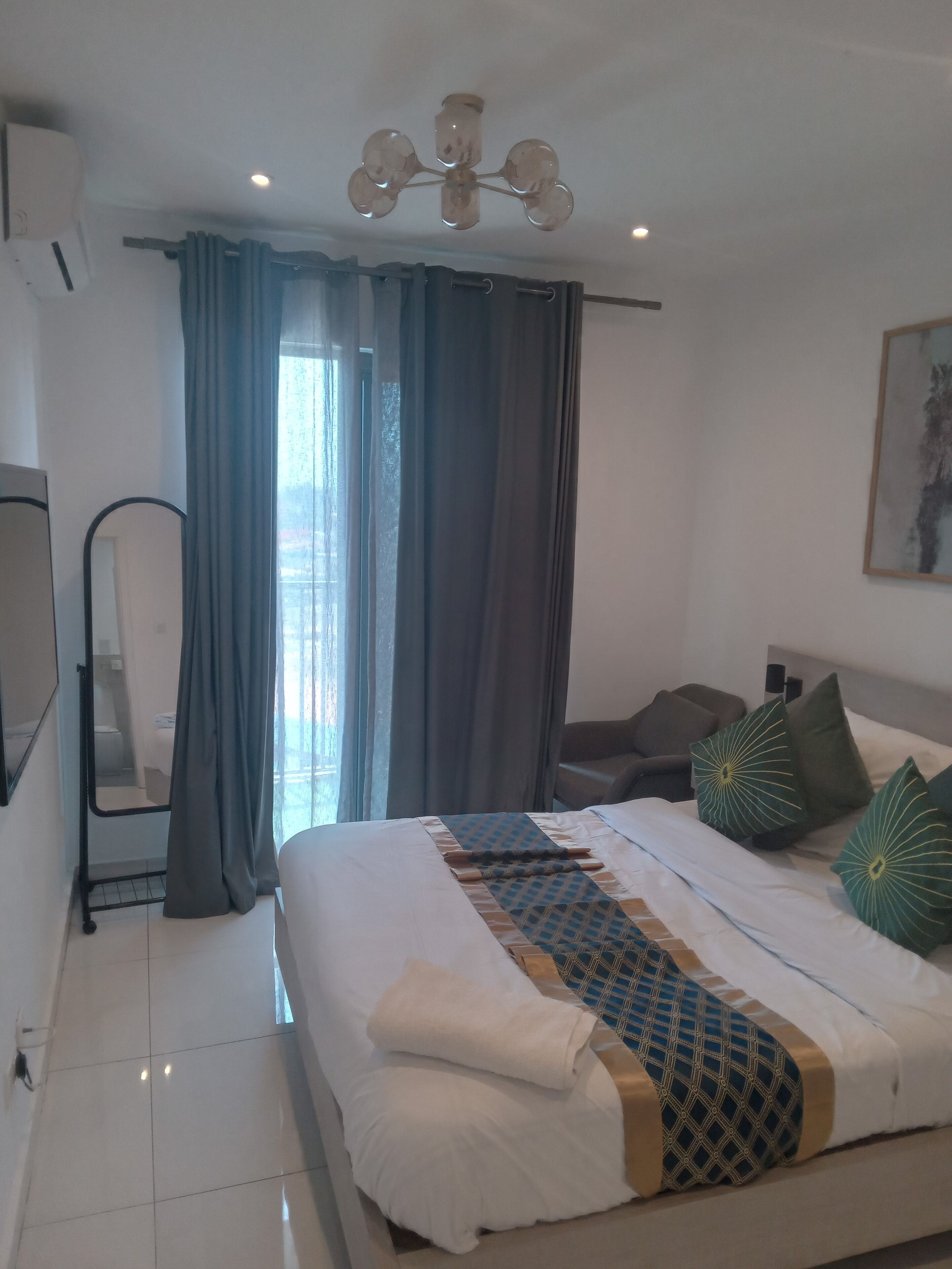 A hotel room with a bed, a chair, a desk, a mirror, and a window with curtains.
