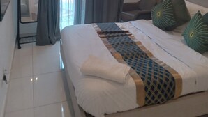 Een hotelkamer met een bed, een stoel, een bureau, een spiegel en een raam met gordijnen.