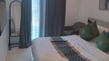 A hotel room with a bed, a chair, a desk, a mirror, and a window with curtains.