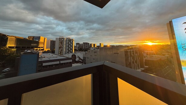 Vista panorámica de la ciudad desde un balcón, con edificios modernos y un atardecer.