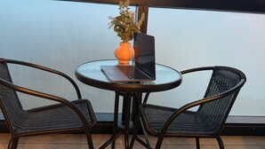 Una mesa redonda de cristal con una computadora portátil y un florero en un balcón con sillas de mimbre.