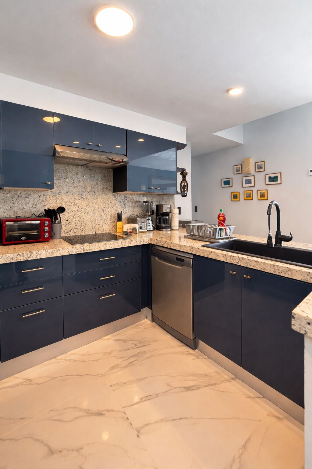 A modern kitchen with dark cabinets, a red toaster oven, a dishwasher, and a granite countertop.