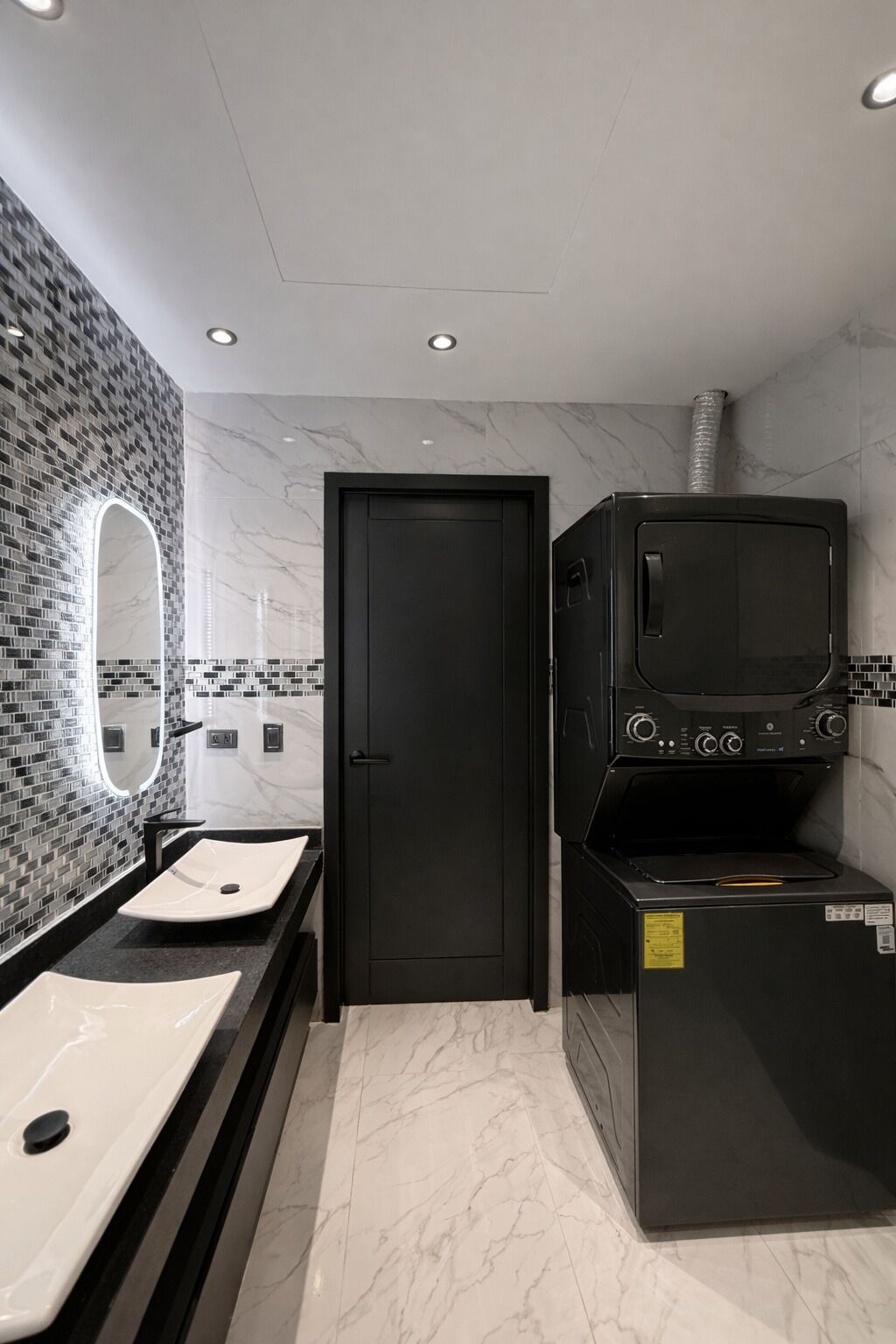 A modern bathroom with two sinks, a large mirror, and a black appliance, possibly a washer and dryer.