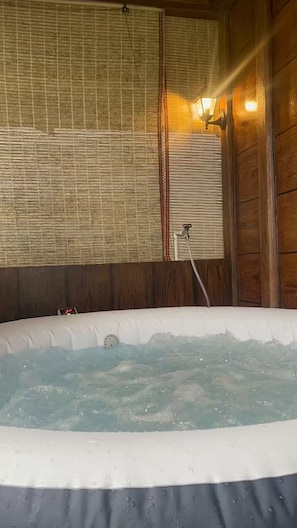 A hot tub with water, a wooden wall, and a window with blinds.