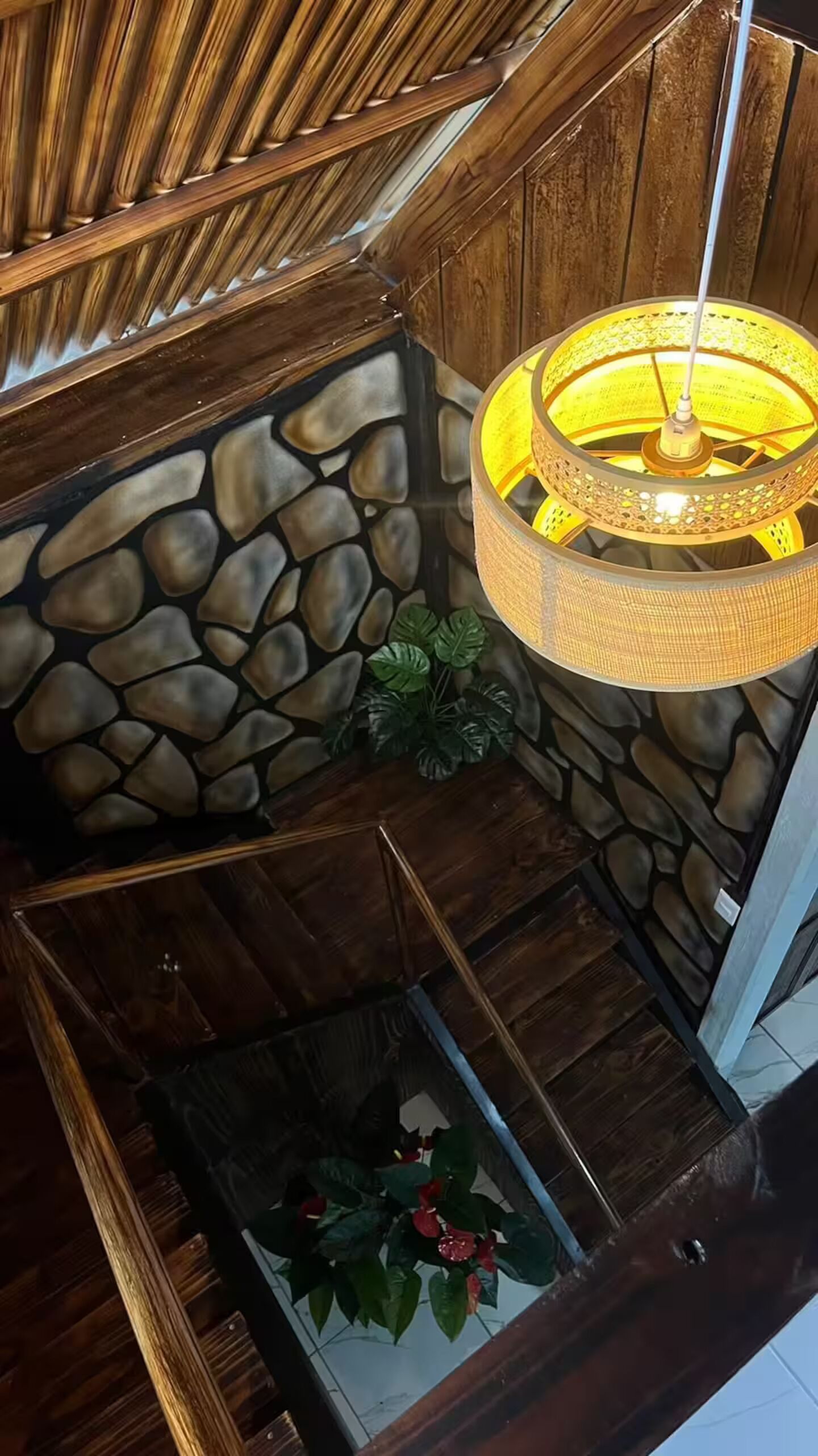 Une pièce avec un mur en pierre, un luminaire suspendu et une plante en pot.