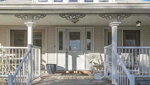 A two-story house with a porch, white railings, and a front door with a window.