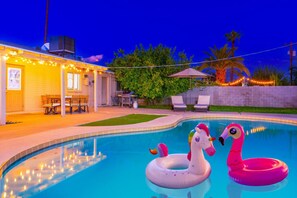 Ein Schwimmbecken mit aufblasbaren Spielzeugen, eine Terrasse mit Stühlen und ein Gebäude mit Lichterketten.