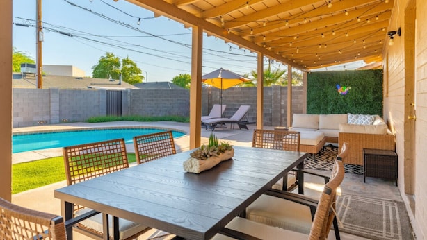 Un patio techado con piscina, mobiliario exterior y un muro verde.