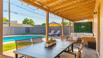 Un patio techado con piscina, mobiliario exterior y un muro verde.