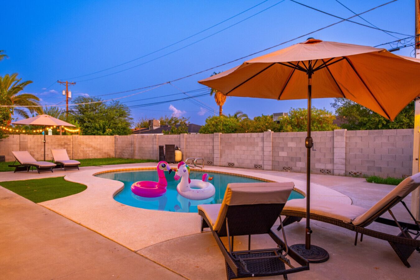 A backyard with a swimming pool, lounge chairs, and inflatable toys.