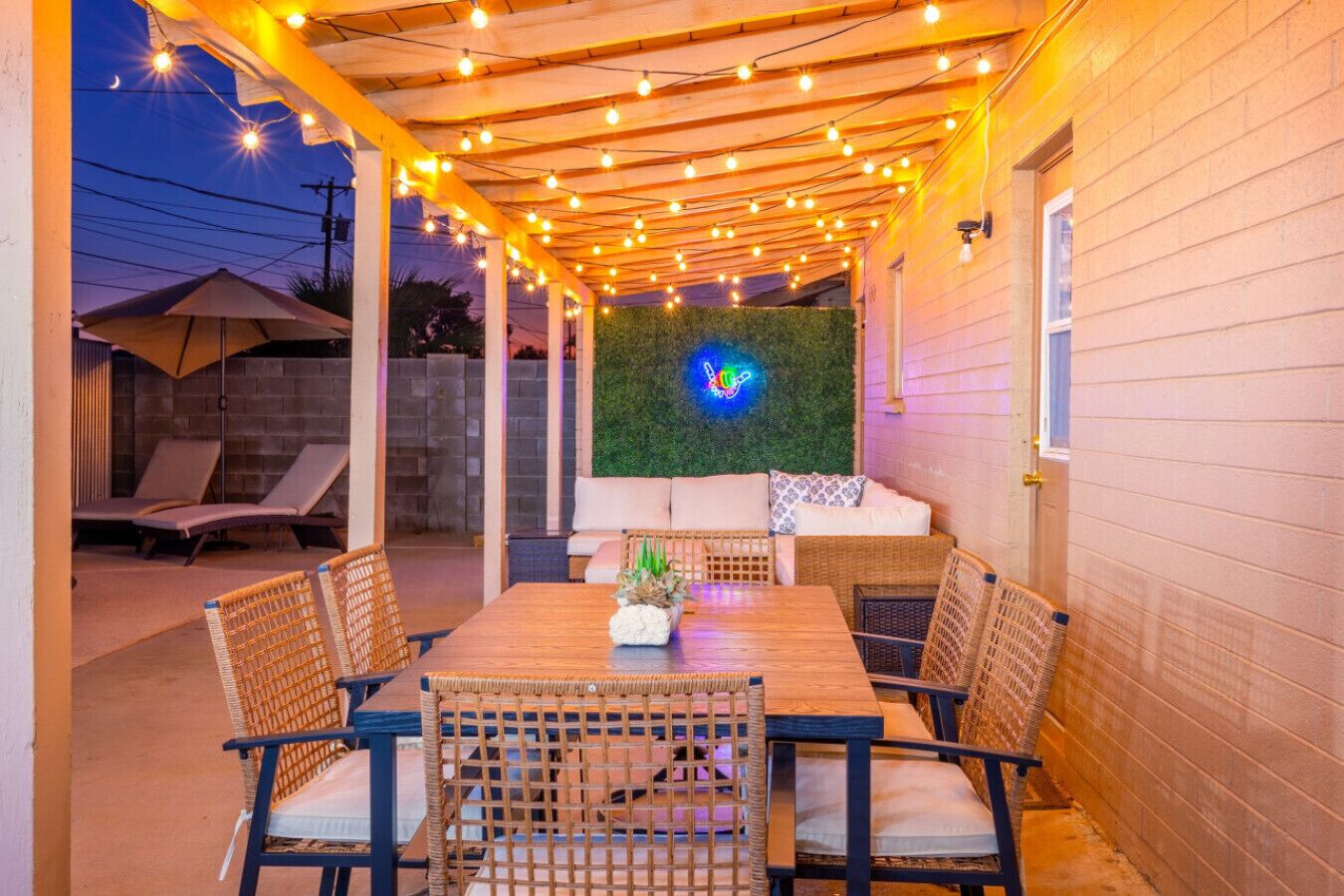 Eine Außenpatio mit Holztisch und Korbstühlen, einer grünen Wand und Lichterketten.