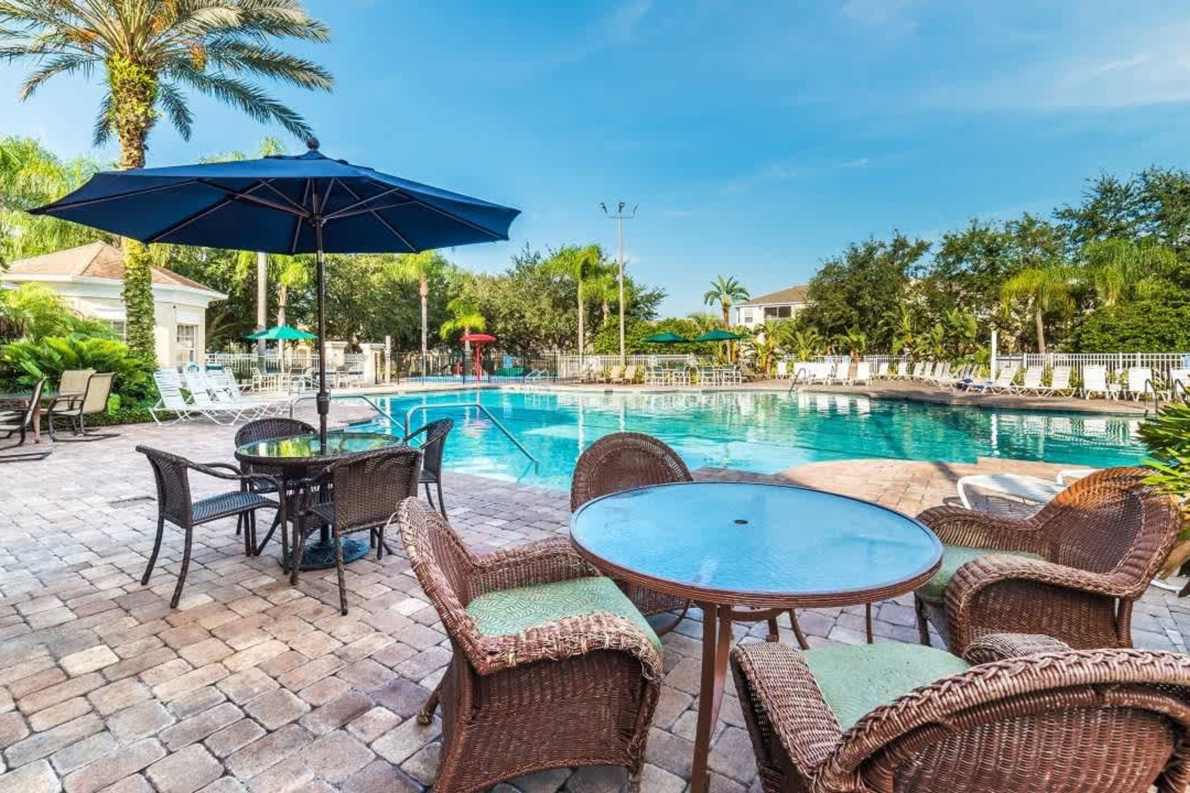 A pool area with wicker furniture, a glass table, and umbrellas.