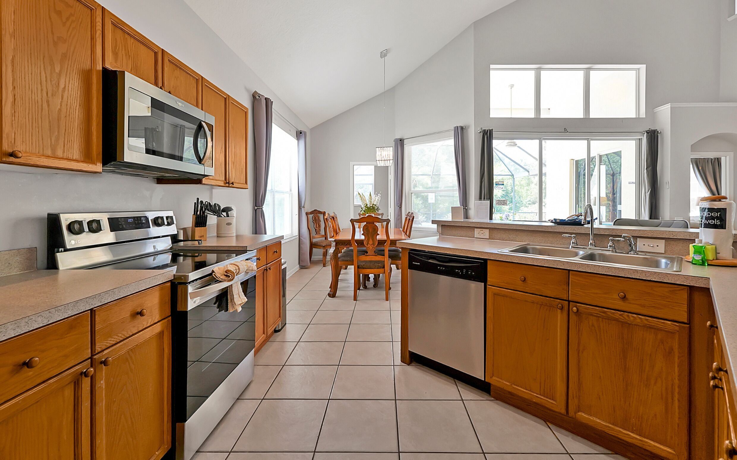 A kitchen with wooden cabinets, a microwave, an oven, a dishwasher, and a dining area with chairs and a table.