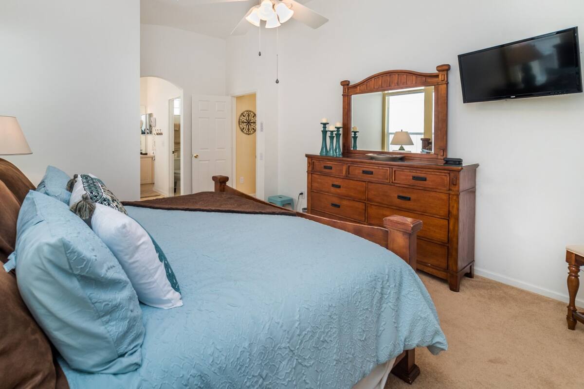 Une chambre à coucher comprenant un lit, une commode, un téléviseur et une porte donnant sur une autre pièce.