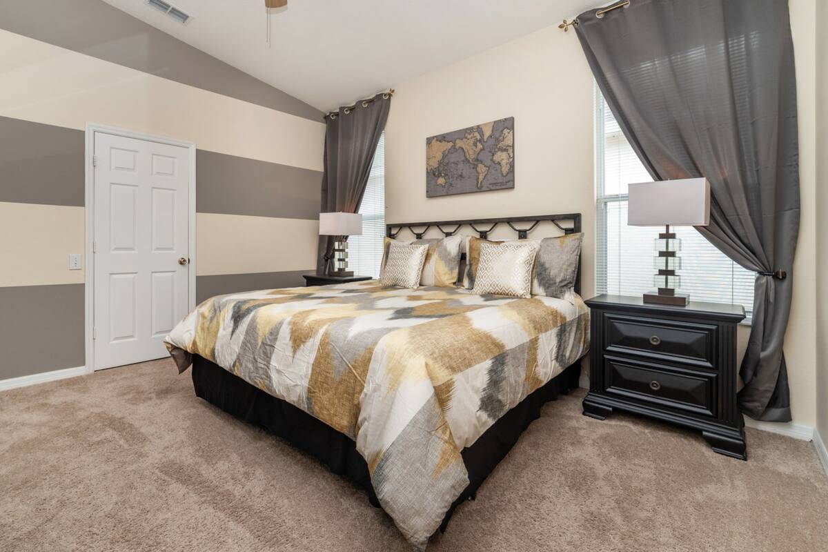 Une chambre à coucher comprenant un lit, deux tables de chevet, une commode, une fenêtre avec des rideaux, une porte et une carte accrochée au mur.