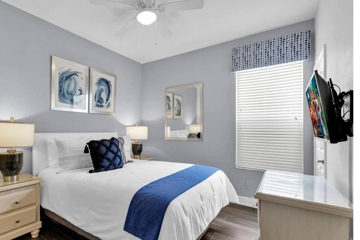 Une chambre à coucher comprenant un lit, deux tables de chevet, un ventilateur de plafond et des œuvres d’art accrochées aux murs.