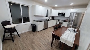 A modern kitchen with white cabinets, stainless steel appliances, a wooden dining table, and a window.