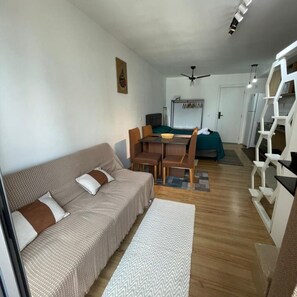 A modern living room with a sofa, dining table, and chairs, a kitchen area, and a staircase.