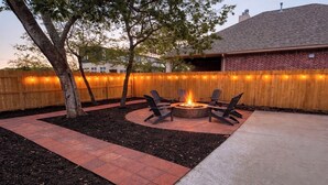 A backyard with a fire pit, chairs, and a wooden fence.