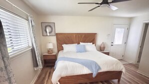 A bedroom with a wooden bed, a ceiling fan, a nightstand with a lamp, and a window with blinds.
