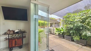 Una habitación moderna con una puerta corrediza de vidrio que da a un patio exterior, un televisor de pantalla plana montado en la pared y un carrito de madera con cristalería.