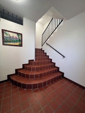 A staircase with a handrail, a painting on the wall, and a tiled floor. - Enjoy your private tropical terrace by the Condado lagoon. (San Juan)