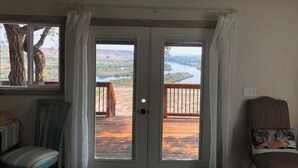 A room with a view of a river and hills, a wooden deck outside, and a chair with a fox pillow. - Rustic Updated Cabin located on the Cliffs of the Snake River (Marsing)