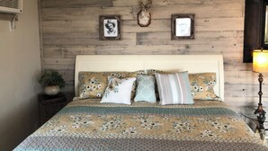 A bedroom with a wooden headboard, floral bedding, a mounted deer head, and a framed picture. - Rustic Updated Cabin located on the Cliffs of the Snake River (Marsing)