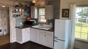A kitchen with white cabinets, a sink, a microwave, and a refrigerator. There is a window with a view of the outdoors. - Rustic Updated Cabin located on the Cliffs of the Snake River (Marsing)