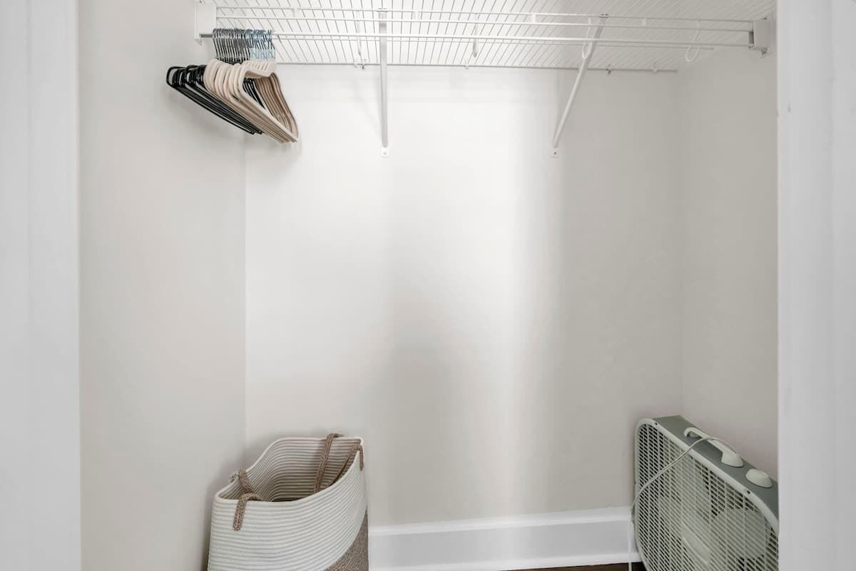 Een witte kamer met een metalen rek, een gevlochten mand en een witte radiator.