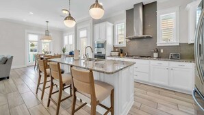 Una cocina moderna con una isla grande, armarios blancos e iluminación colgante.