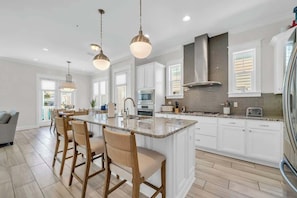 A modern kitchen with a large island, white cabinetry, and pendant lighting. - Freedom On 30A by Stay on 30a (Inlet Beach)