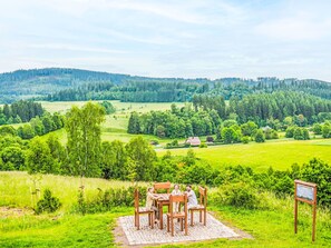 Una familia cenando en una mesa con vistas a un valle exuberante y colinas boscosas al fondo.