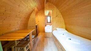Interior acogedor de una cabaña de madera con una cama individual, una mesita y un banco.