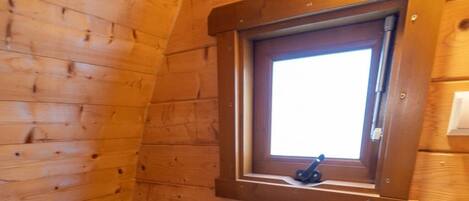 A small, wooden-paneled bathroom with a toilet, sink, and a window above the sink.