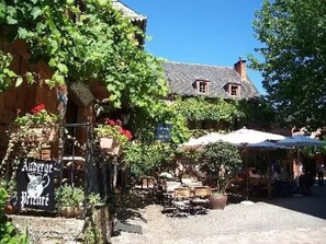 A courtyard with outdoor seating, a sign for a restaurant, and a building with a sloped roof.