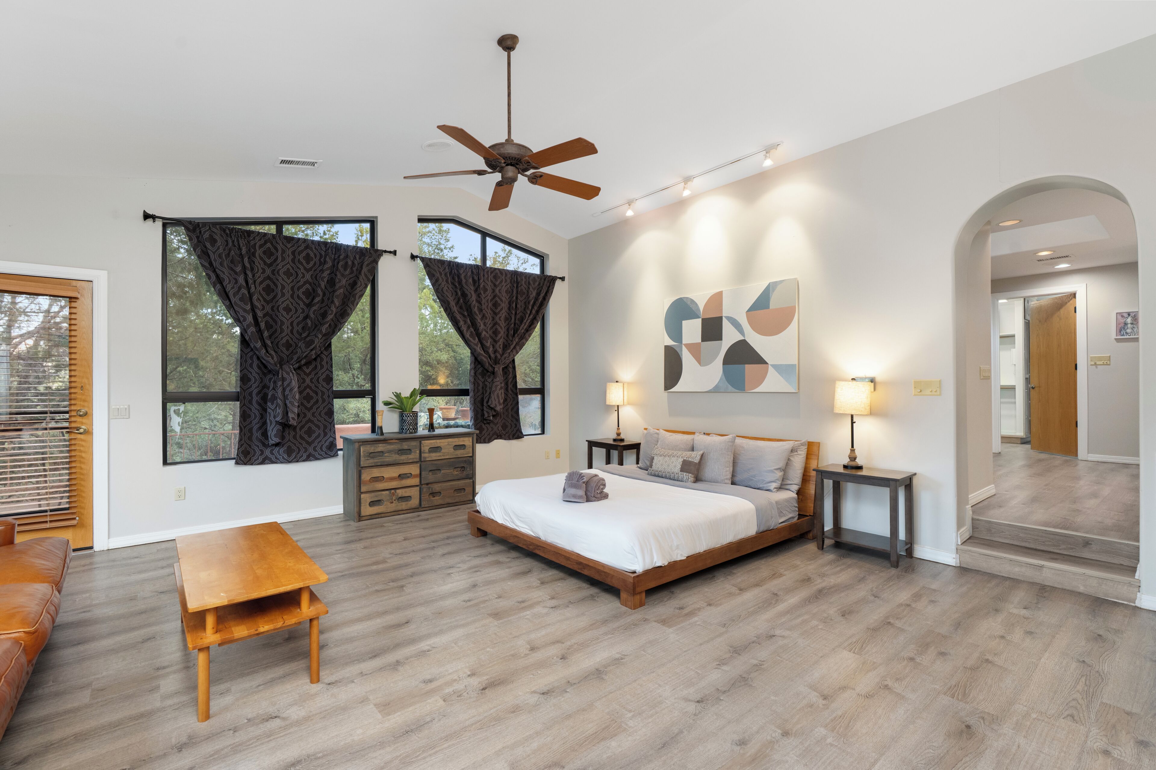 A bedroom with a bed, wooden furniture, a ceiling fan, and a large window with curtains.