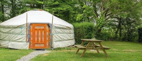 A yurt with a wooden door, a picnic table, and a gravel path leading to it.