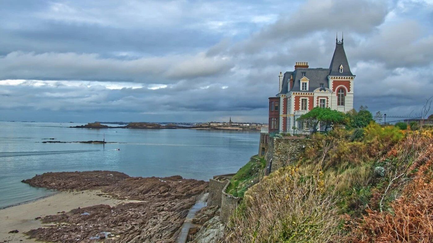 A historic building with a prominent tower, situated by a rocky shoreline with a view of the sea.
